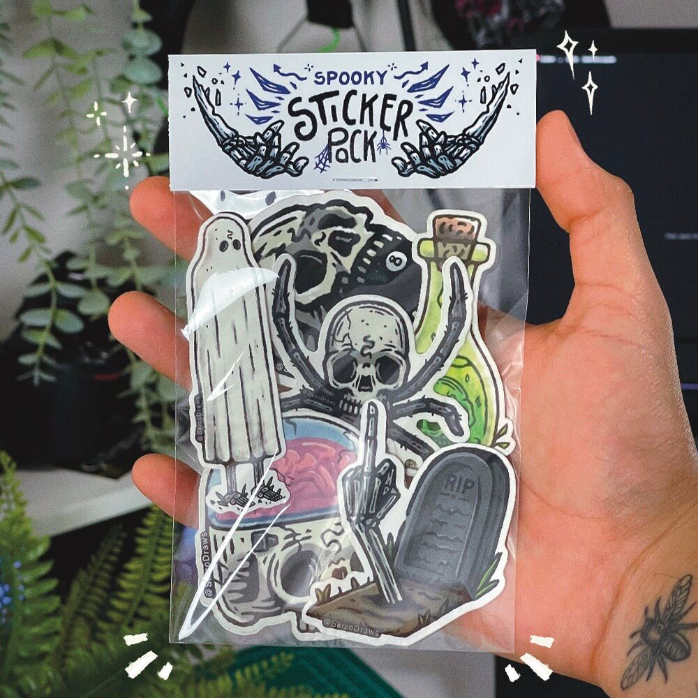 En hånd som holder en stickerpakke med tegnede klistremerker i skummelt tema og en header der det står «SPOOKY STICKER PACK», mot en bakgrunn av planter