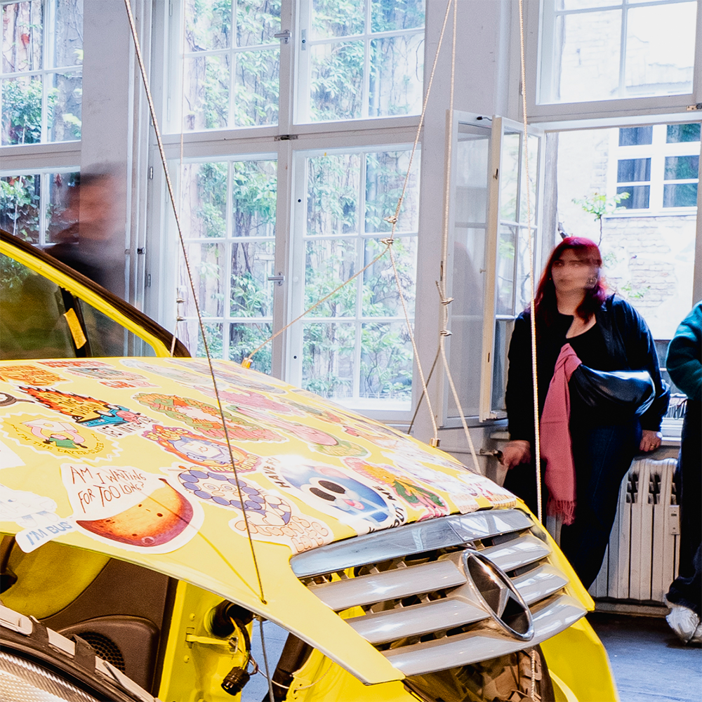 Yellow Mercedes body covered in bumper stickers in various shapes and sizes, with a german licence plate.