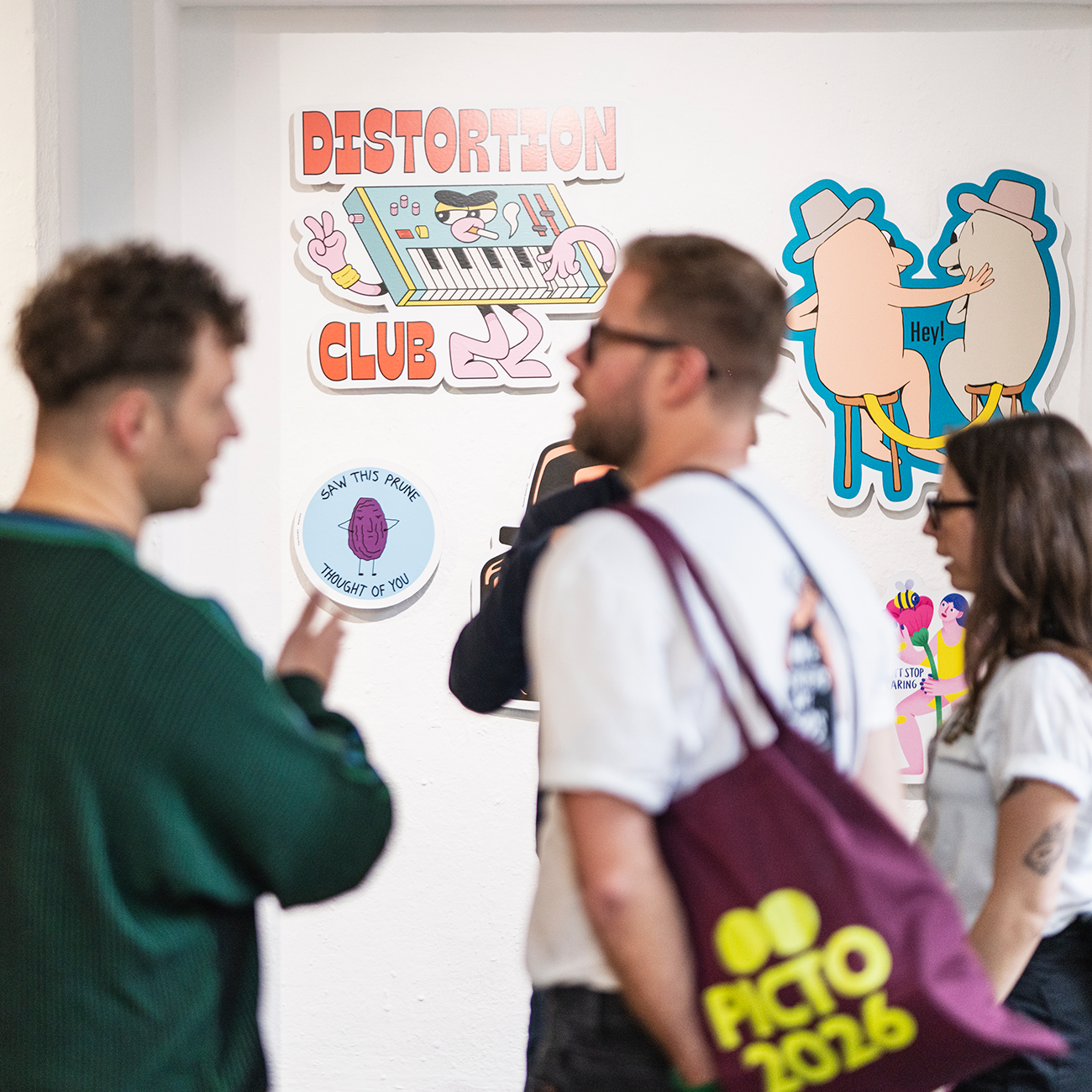 Visitors at an art exhibition talking, behind them artwork hanging on display, with the text "Distortion Club".
