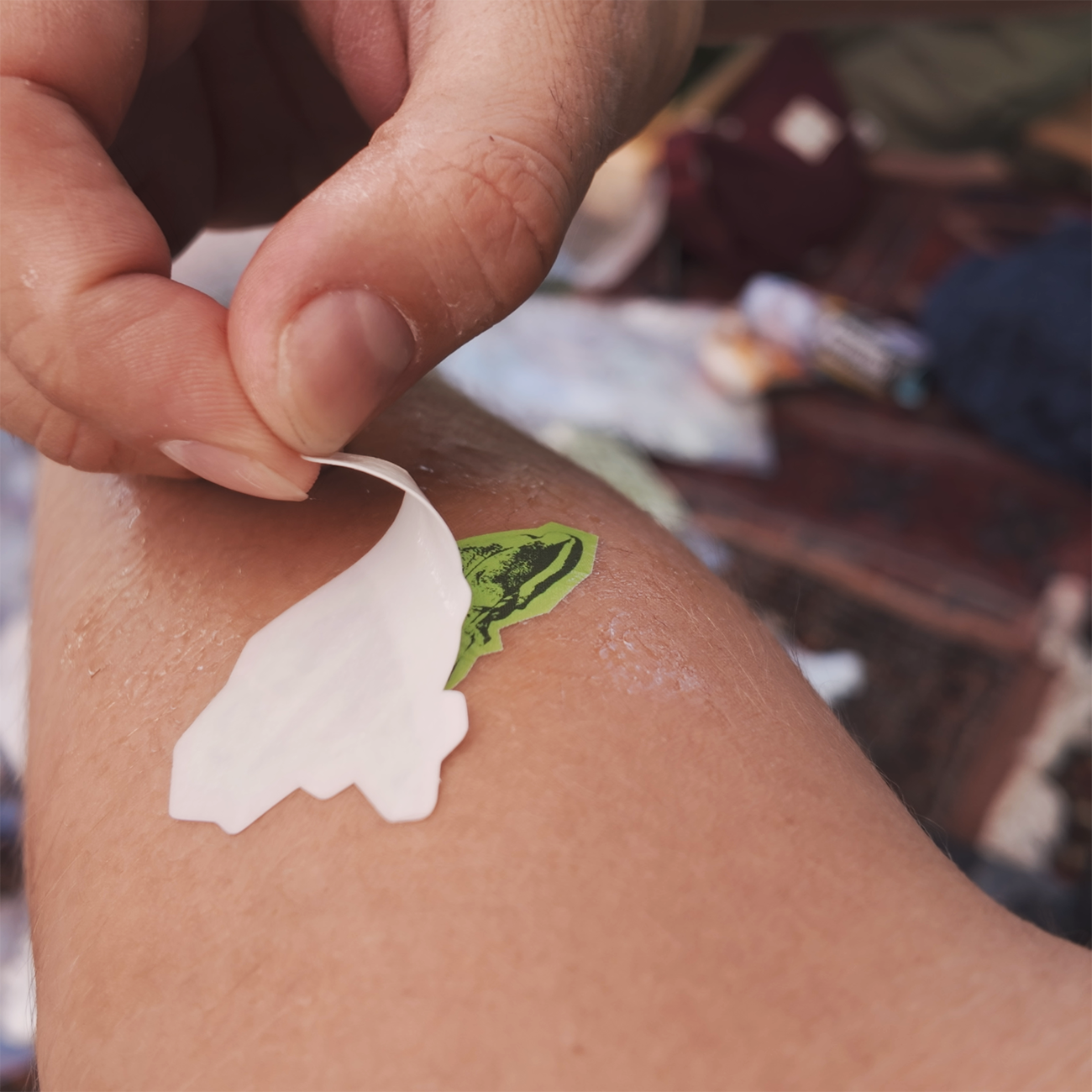 Die-cut temporaty tattoo in light and dark green, placed on an arm with the backing film peeled