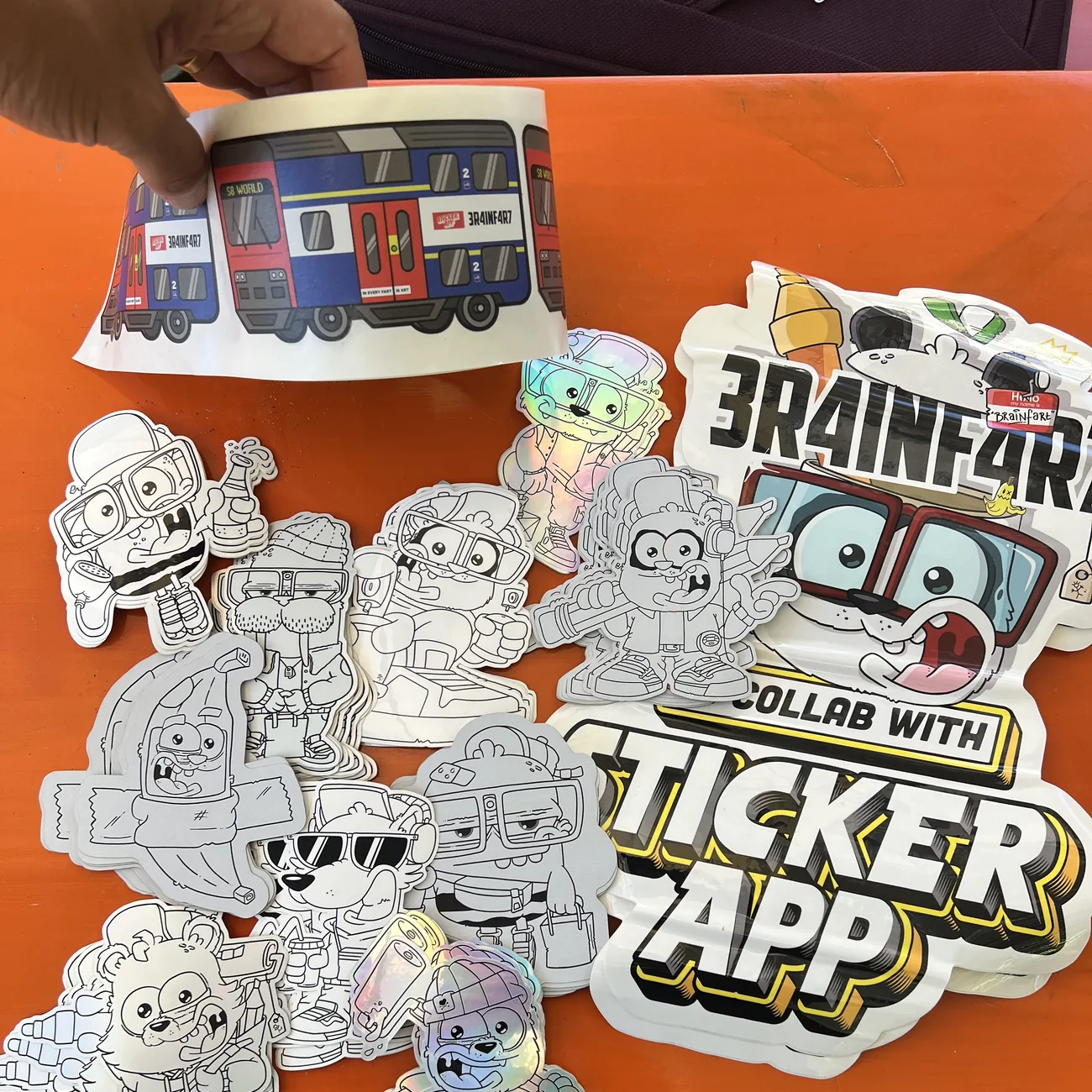 Etikett med S8 World-toget fra Brainfart x StickerApp med skiltet "In every fart is art", holdt over svart-hvite die-cut klistremerker