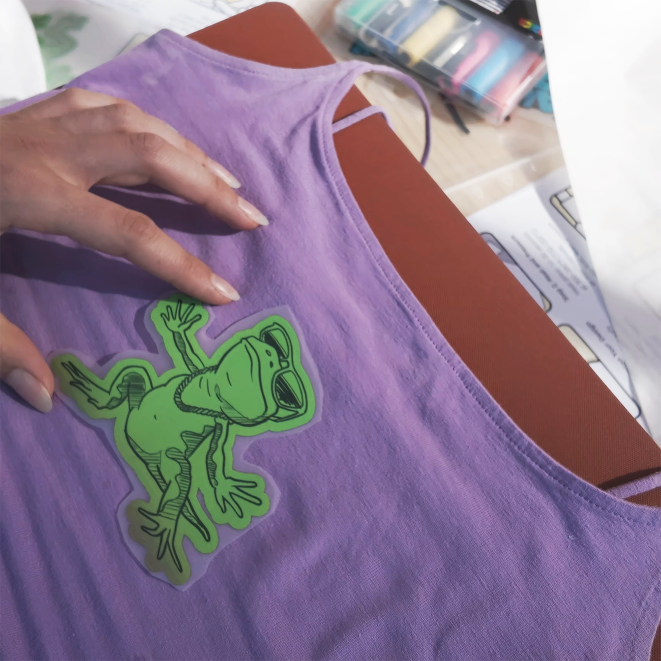 Die-cut DTF heat transfer print of a dark and light green frog placed on a purple garment with a heat press