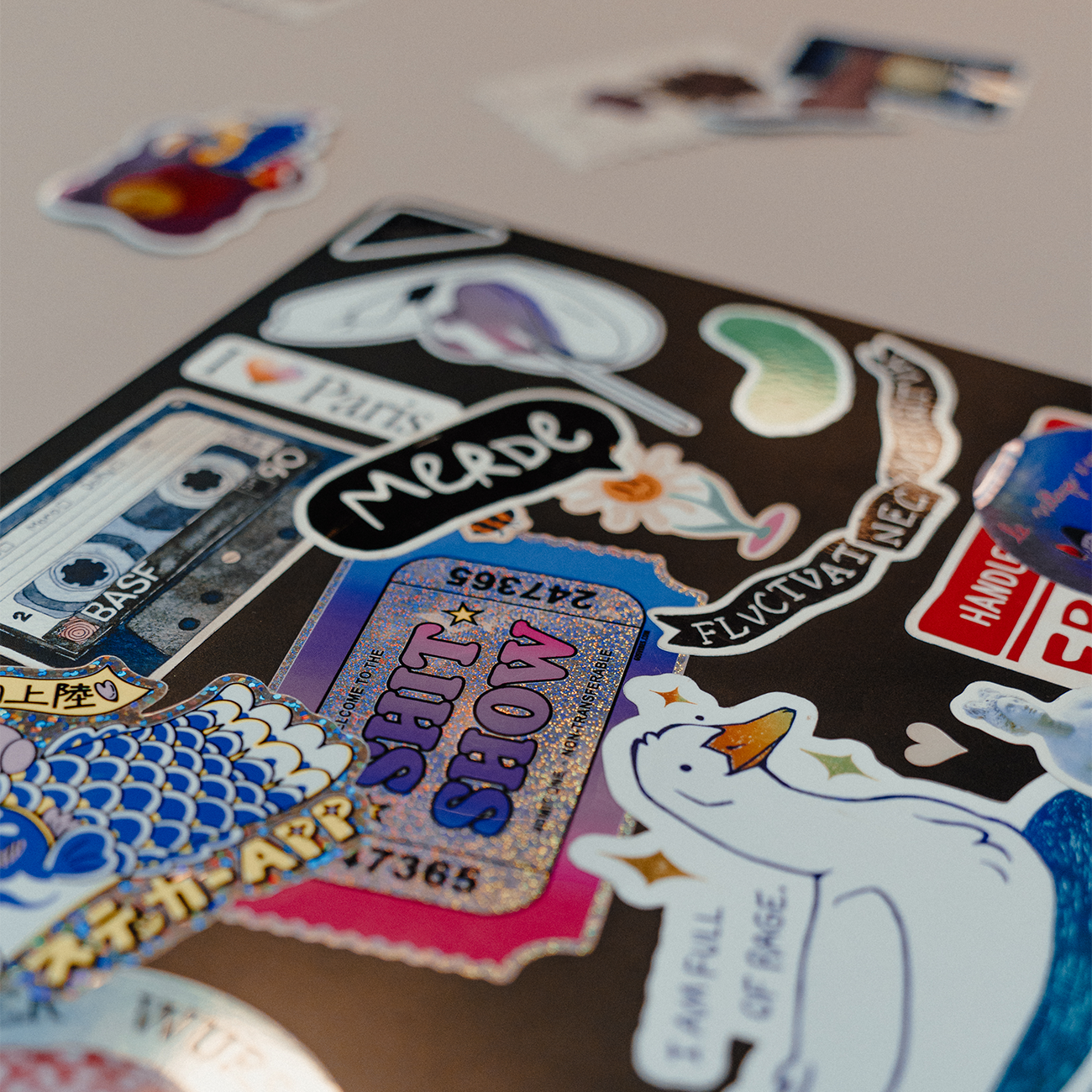 Laptop covered in a variety of colorful stickers, including illustrations, text-based designs, and graphics, placed on a table with loose stickers scattered in the foreground.