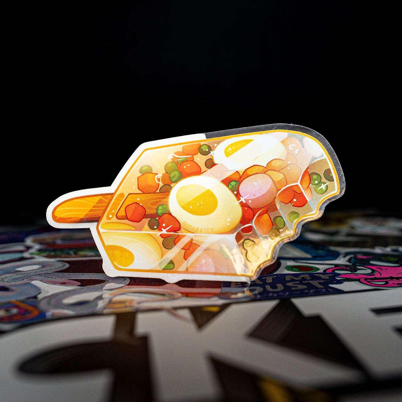Egg and peas formed as a popsicle, with a wooden handle and colorful artwork in the foreground against a black bakground.