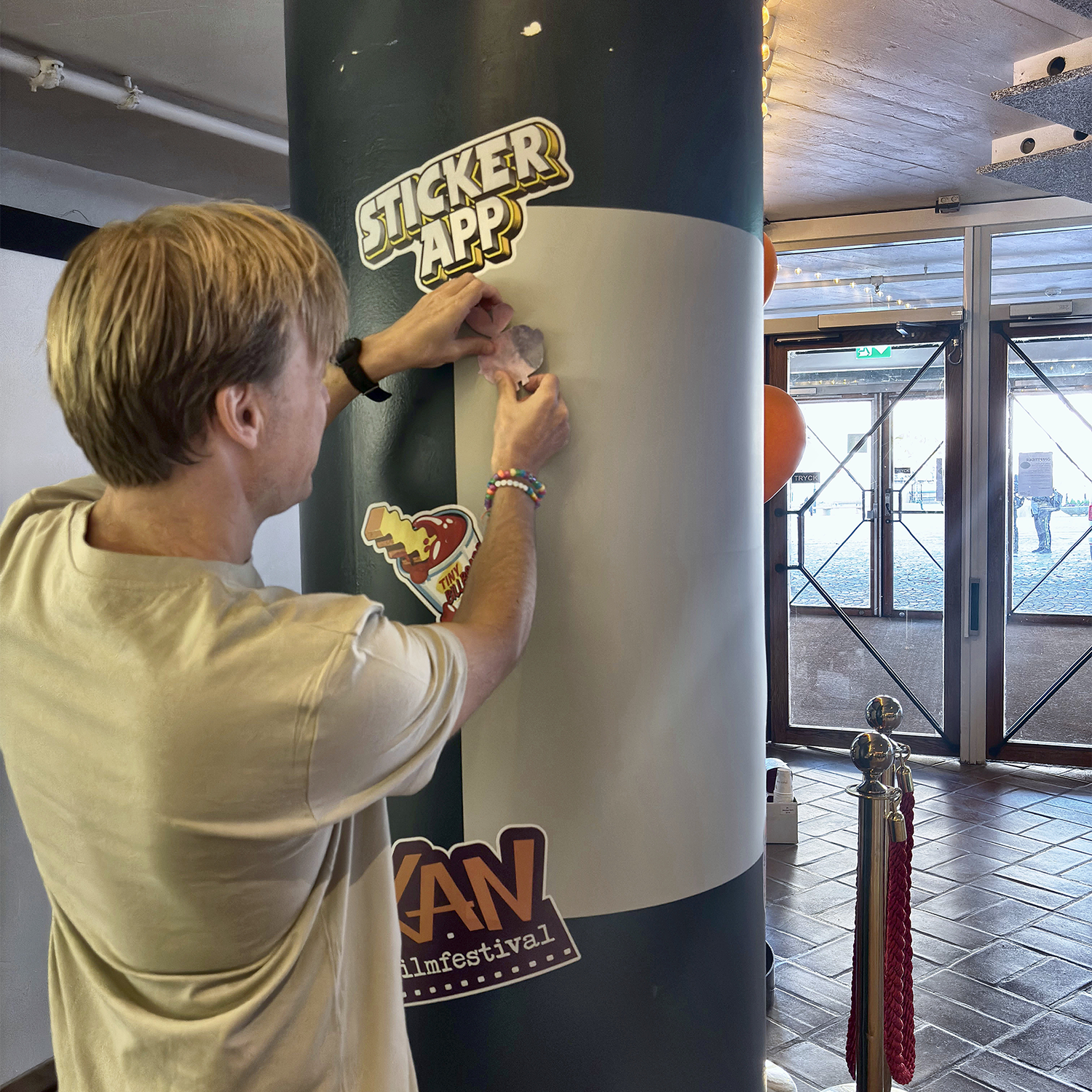 Mann som setter et klistremerke på StickerApps klistremerkevegg rundt en søyle på KAN filmfestival