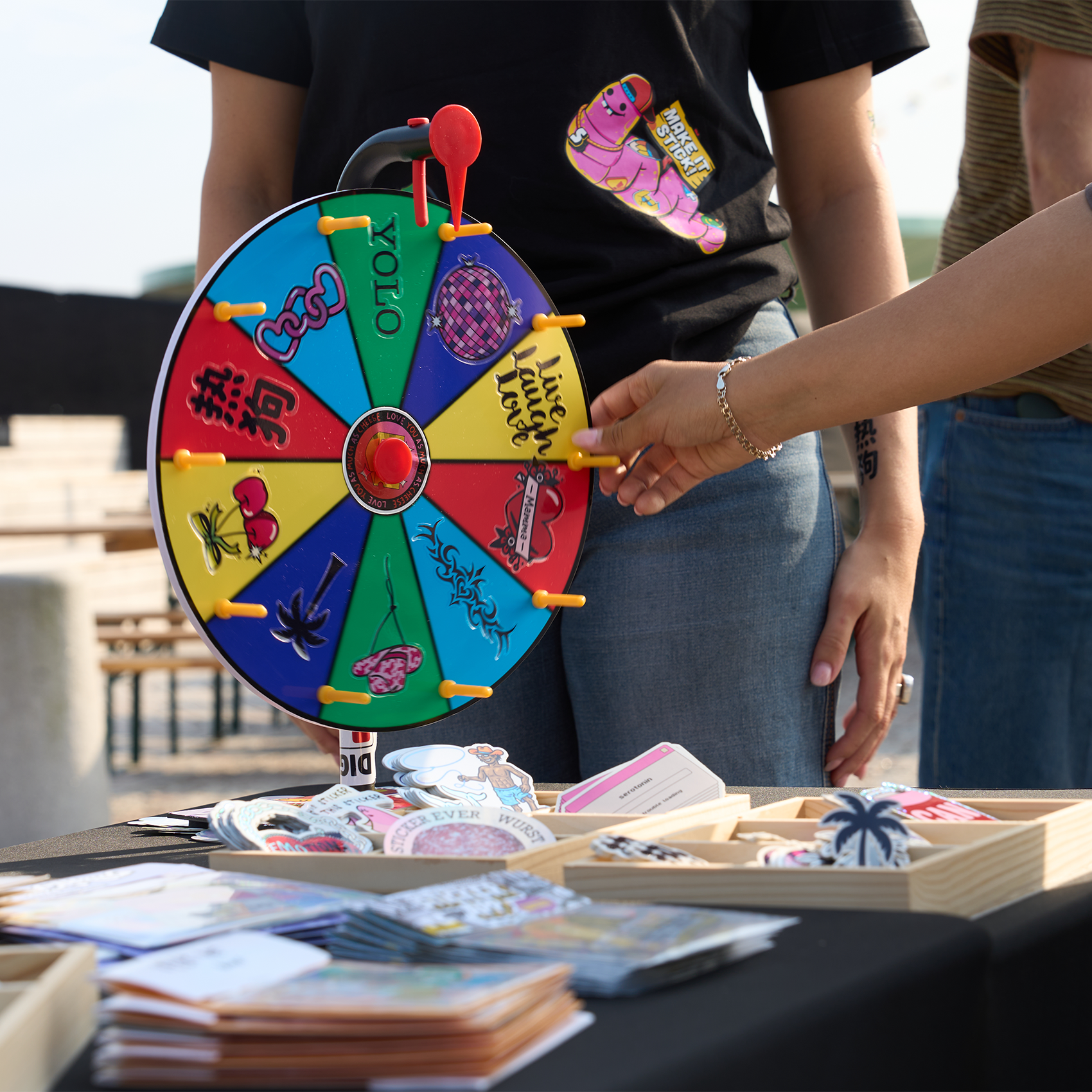 Person spinning a colorful prize wheel at a sticker and temporary tattoo stand