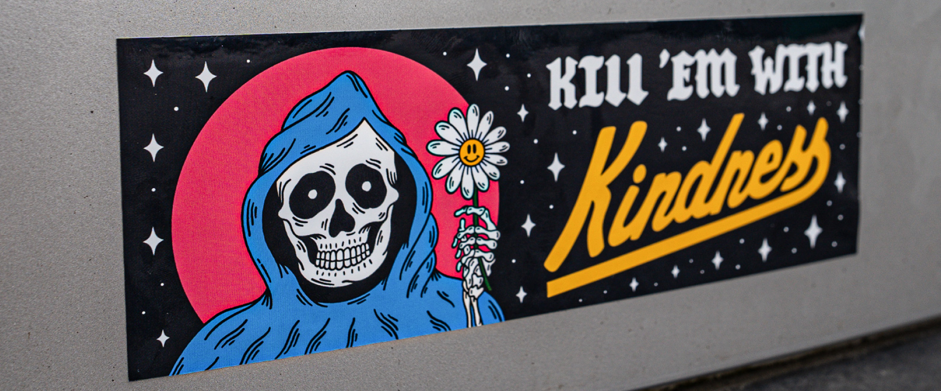 A bumper sticker with a skeleton holding a flower, Kill 'em with kindness.