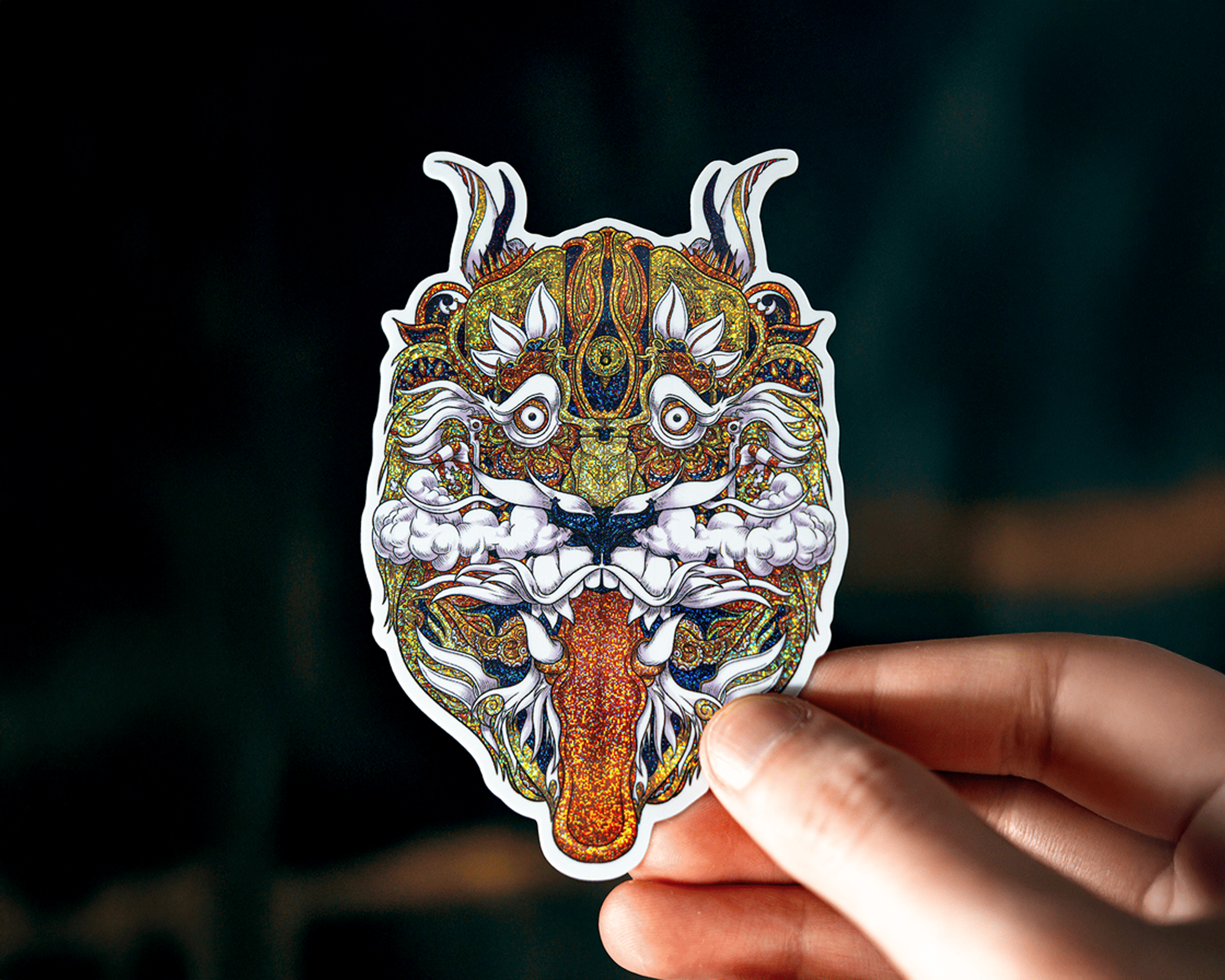 Hand holding a colorful, intricately designed tiger pixie dust sticker with exaggerated features and vivid patterns against a dark background.
